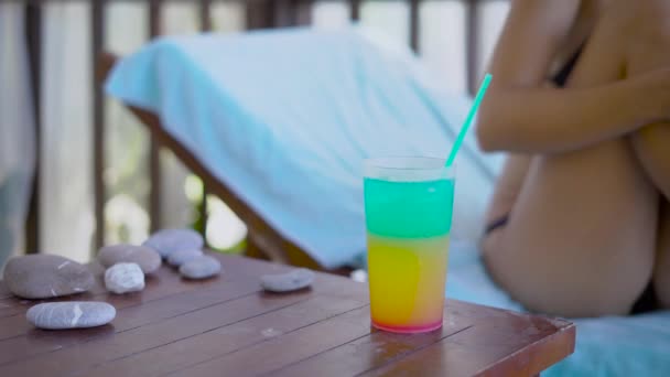 Slanke lichaam van jonge vrouw draagt in zwarte bikini zit op een zonnebank in de zomerdag, vrouw hand neemt glas met cocktail — Stockvideo