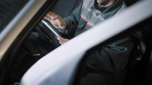 Mécanicien assis dans une voiture avec une tablette . — Video