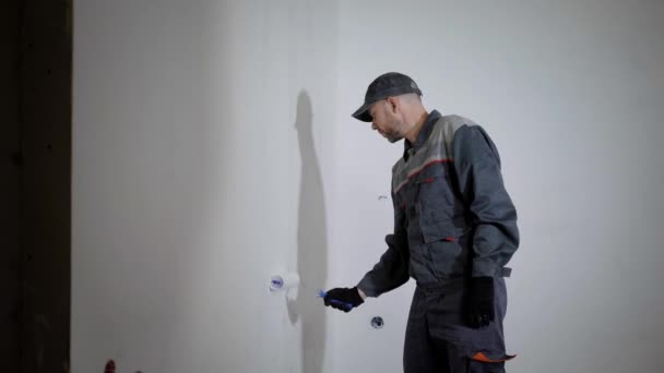 Профессиональный художник носит рабочую форму и колпачок покраски стены за роликом с белым цветом, вид сбоку — стоковое видео