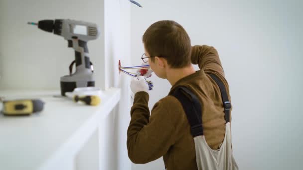 Elektricien is knippen van draden en proberen op een socket mechanisme verzonken in een witte muur in flat in reparatie — Stockvideo