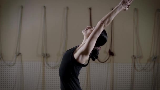 Mujer deportiva con el pelo oscuro está de pie en una sala de gimnasia, haciendo ejercicios de respiración y la práctica de estiramiento — Vídeos de Stock