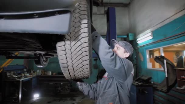 Mécanicien de voiture est d'enlever une roue de voiture relevée, debout sur un plancher, regarder et vérifier le disque dans un garage — Video