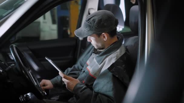 Technicien automobile vérifie la boîte de vitesses, déplace la vitesse et regarde sur un écran d'ordinateur de voiture, assis à l'intérieur d'une voiture, entrer des données dans une tablette — Video