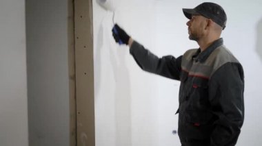 Çalışan formunda profesyonel adam daire duvar boyar, builder bir rulo elinde tutar.