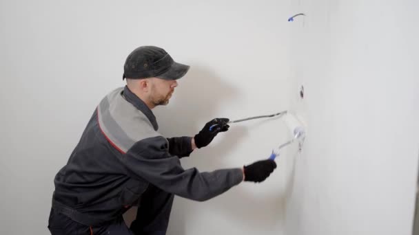 Un joven constructor trabaja en la instalación, un hombre hace reparaciones, la gente usa pintura y un rodillo para pintar paredes — Vídeos de Stock