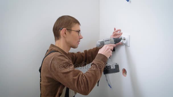 Um retrato de um eletricista que instala um soquete, um homem segura uma broca elétrica e parafusos — Vídeo de Stock