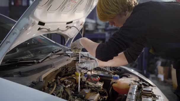 Un joven está girando con la ayuda de una herramienta el motor de un mecánico de automóviles está reparando el coche con el fin de que vaya bien — Vídeos de Stock