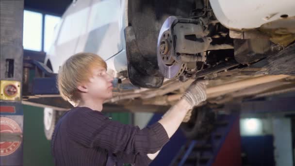 A young male mechanic engaged in repairing the wheels of the vehicle, he checks the clutch for good braking — Stock Video