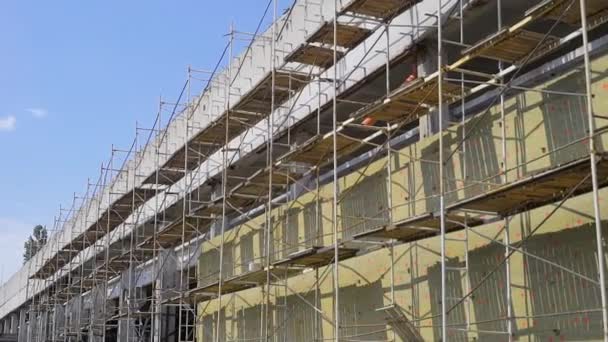 Scaffolding is fixing along the wall of the renovated industrial building in sunny weather, camera is moving — Stock Video