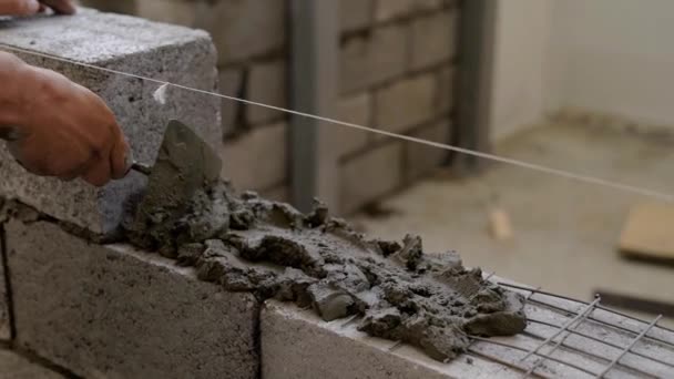 Trabajador está aplicando mortero de cemento en una pared para colocar bloques de construcción, distribuyendo uniformemente, utilizando espátula — Vídeo de stock