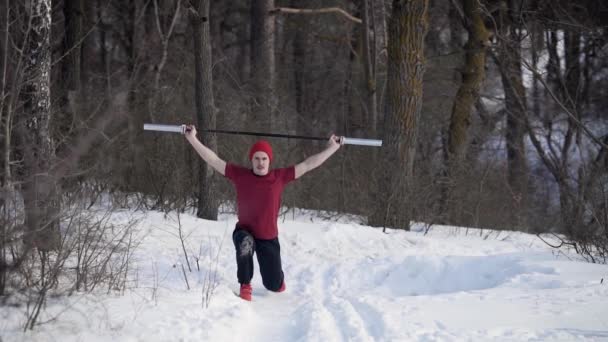 Jovem desportista com haste levantada sobre a cabeça está fazendo lunges por pernas em uma floresta de inverno nevado de manhã — Vídeo de Stock