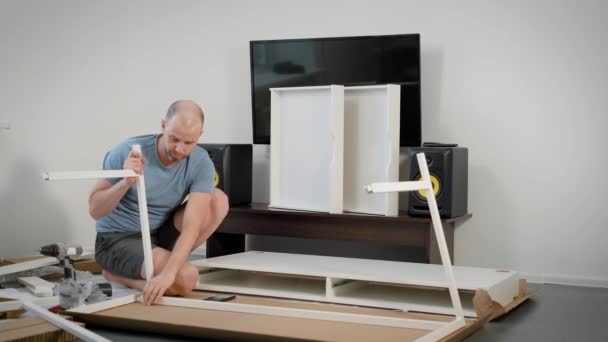 Хлопець сам збирає меблі в кімнаті, встановлюючи довгі білі балки на тушу сучасного столу — стокове відео