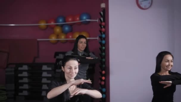 Três mulheres morenas estão fazendo exercícios corporais em uma sala de ginástica, olhando para a frente e repetindo para o treinador — Vídeo de Stock