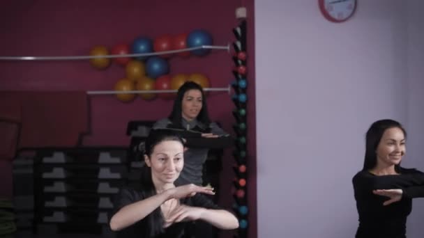 Tres mujeres morenas están haciendo ejercicios corporales en una sala de gimnasia, mirando hacia adelante y repitiendo para entrenador — Vídeos de Stock