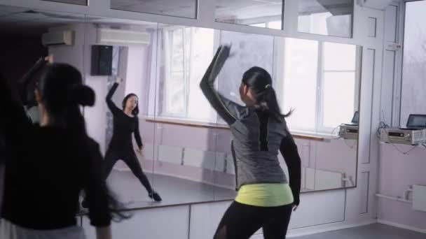 Tres mujeres activas están bailando en una sala de deporte frente a una pared de espejo, saltando vigorosamente y levantando las manos — Vídeos de Stock