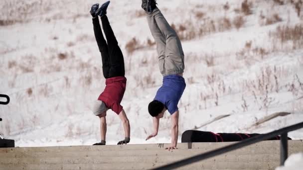 Δύο Αθλητικός άνδρας πηγαίνει κάτω κάνει ένα handstand εξωτερική το χειμώνα. — Αρχείο Βίντεο