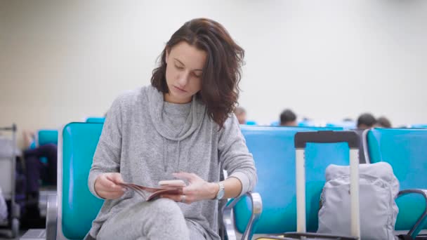 Woman is checking data in her passport and in a ticket on airplane in a waiting hall of aeroport, registering online — Stock Video