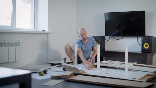 Pro dospělé holohlavý muž nosí domů oblečení je montáž nábytku v bytě. — Stock video