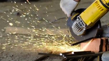 Oluşturucu el ateş yakın, metal ile çalışmak için bir testere tutan kişi bir adam metal çubuk bir parça inşaat alanı üzerinde keser.