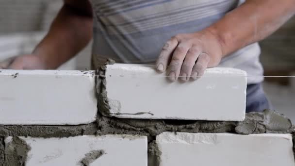 Close shot at the builder hands, the man puts the bricks on concrete, for evenness he uses a rope, he beats a spatula on the rocks — Stock Video