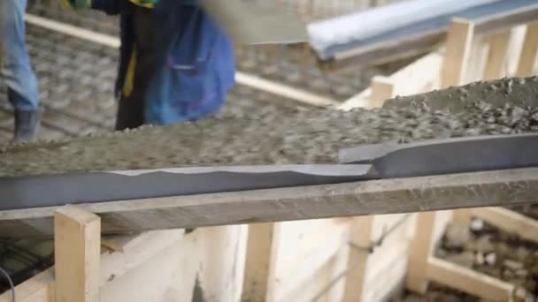 Een nauwe beschoten de heuvel op welke vloeistof beton of cement invoert, een man duwt het materiaal met een schop, het vuil valt op de toekomstige Stichting — Stockvideo