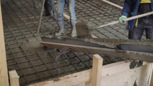 Близкий выстрел по самодельному холму, на который входит бетон или цемент для создания пола на строительной площадке, строители работают с лопатами — стоковое видео