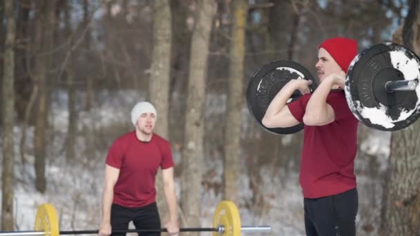 2 人の友人は冬の日、自然にスポーツのために行く、彼は重い負荷でバーを持ち上げる、男性は積極的にスポーツのために行く — ストック動画