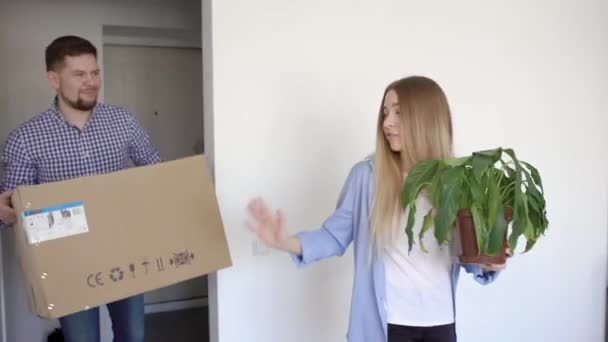 Een jonge vrouw draagt een bloem in haar hand, haar man draagt een vak, het paar verhuisde naar een nieuw appartement — Stockvideo