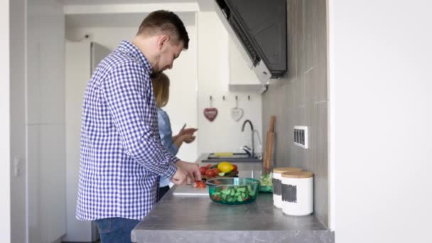Jovem mulher e seu homem adulto preparando uma salada de legumes frescos, um par de lavagens e cortes de legumes — Vídeo de Stock