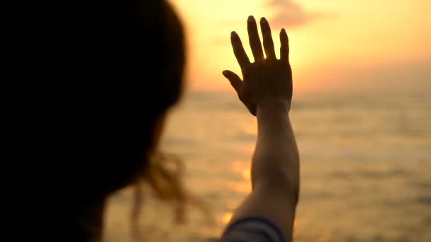 The woman enjoys the sunset and stretches her hand to the sun, the silhouette of the fingers that the lady moves — Stock Video