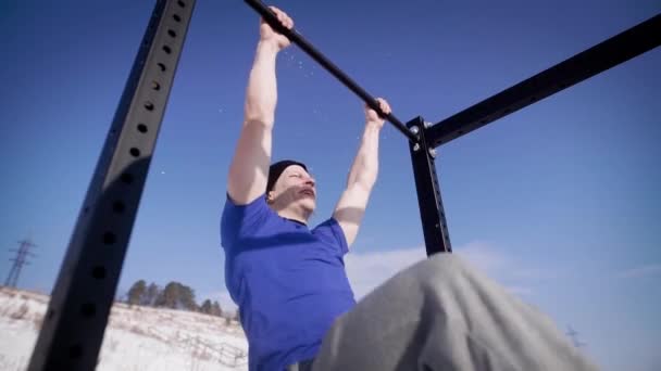 Junger muskulöser Mann macht Klimmzüge am Stab, während er in der verschneiten Natur trainiert — Stockvideo