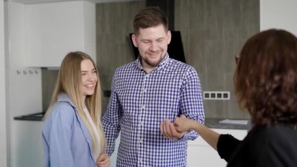 Realtor dando chaves para alegre mover-se no homem e na mulher enquanto está no apartamento — Vídeo de Stock