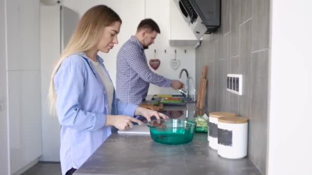 Vista lateral del joven hombre y la mujer de pie juntos en la cocina y la cocina en casa — Vídeo de stock