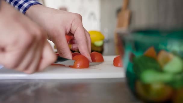Plantaardige onherkenbare man staande aan tafel op keuken en hakken tomaat op snijplank — Stockvideo