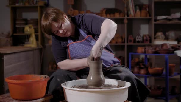 Una mujer joven aprende a crear productos de arcilla, el estudiante trabaja con una rueda de alfarero y material de cerámica húmeda — Vídeo de stock