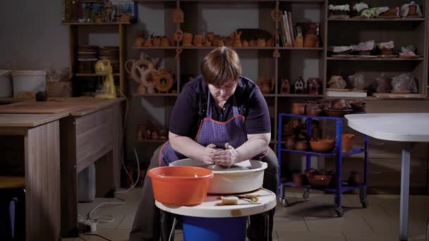 Доросла жінка займається створенням вази з глини, вона сидить за гончарним колесом і формує статтю з глини — стокове відео