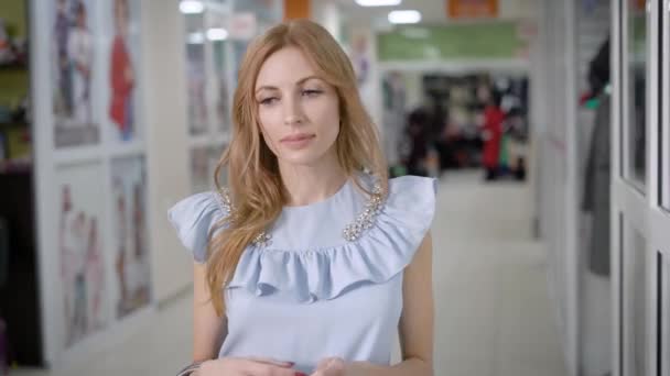 Mujer joven está caminando por el pasillo en el centro comercial durante el día, viendo un maniquí en una vitrina de la tienda de ropa y entrar — Vídeo de stock