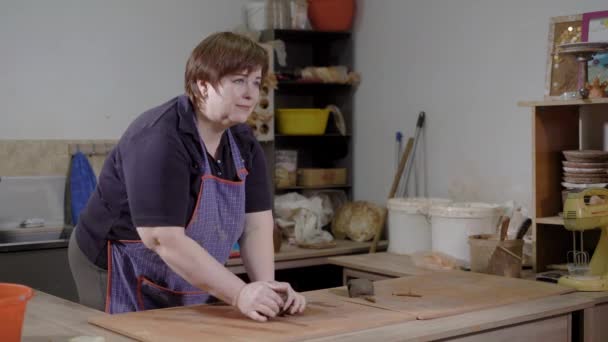 Alfarero mujer adulta está machacando pedazo de arcilla en una mesa en un taller de cerámica, la preparación de la etapa en una fabricación — Vídeos de Stock