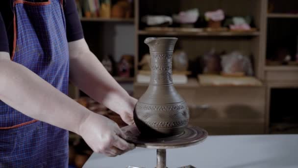 Potter is wearing an apron is putting new fresh clay bowl on a rotating platform in working studio, demonstrating product — Stock Video