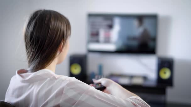 Close up shot from behind of a brunette woman watching tv indoor sitting on sofa. — Stock Video