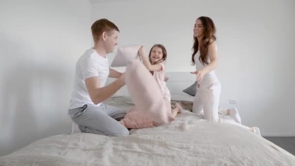 Father mother and little daughter are having a pillow fight indoor on bed. — Stock Video