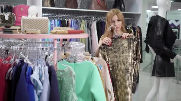 Mulher loira bonita está escolhendo roupas na boutique . — Vídeo de Stock