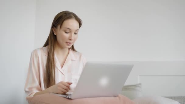 Jovem e bonito mulher falando com amigos em redes sociais segurando laptop em seus pés no quarto — Vídeo de Stock