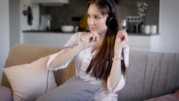 Giovane donna che ascolta musica con le cuffie seduta in soggiorno sul divano, canta e si diverte — Video Stock