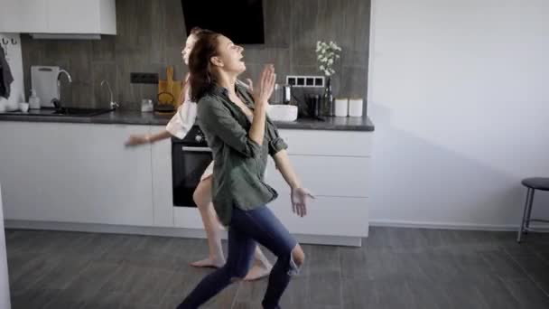 Two young forefathers dance to energetic music in the kitchen, funny women are actively fooling around — Stock Video