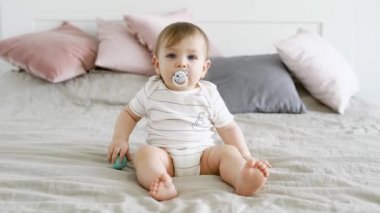 cute, komik çocuk bir emzik ağzında ve topları elinde bir yatakta oturur, çocuk önde görünüyor