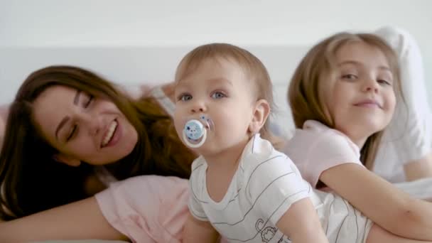Moeder haar pasgeboren kind met zorg behandelt, haar zus en de man naast haar, de familie is liggend op het bed — Stockvideo
