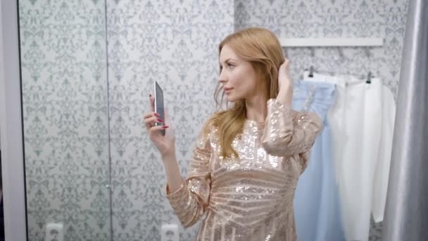 Молодая симпатичная блондинка, глядя в зеркало, делает фотографии на свой смартфон для публикации — стоковое видео
