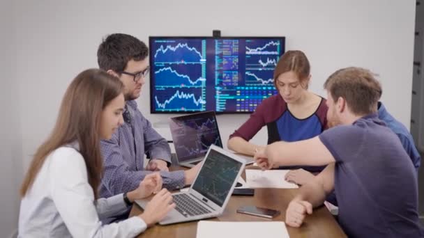 Молоді фінансисти на зустрічі. Чоловіки і жінки обговорюють валютний ринок і стратегію розвитку супутників. Багато індикаторів відображаються в інтерактивних панелях . — стокове відео