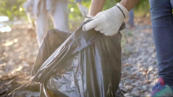 Vista close-up de saco de plástico com lixo na floresta, as pessoas estão colocando resíduos nele, território de limpeza — Vídeo de Stock